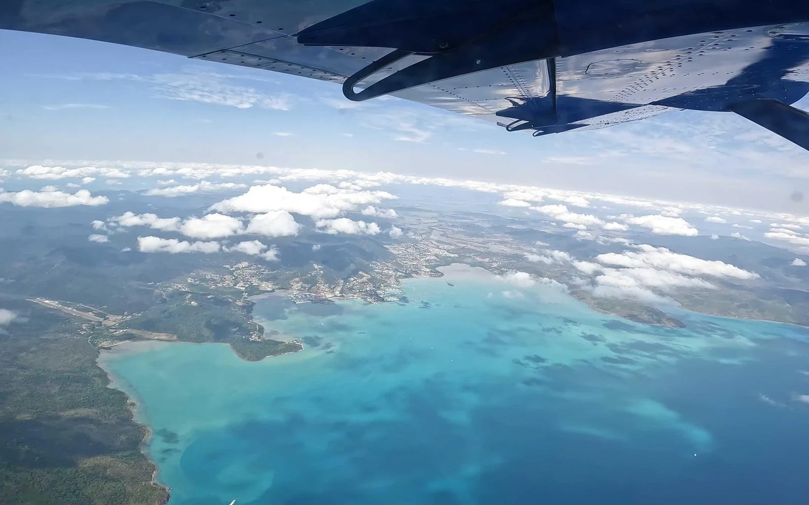 从机翼旁俯瞰Airlie Beach的海岸线与碧绿浅滩